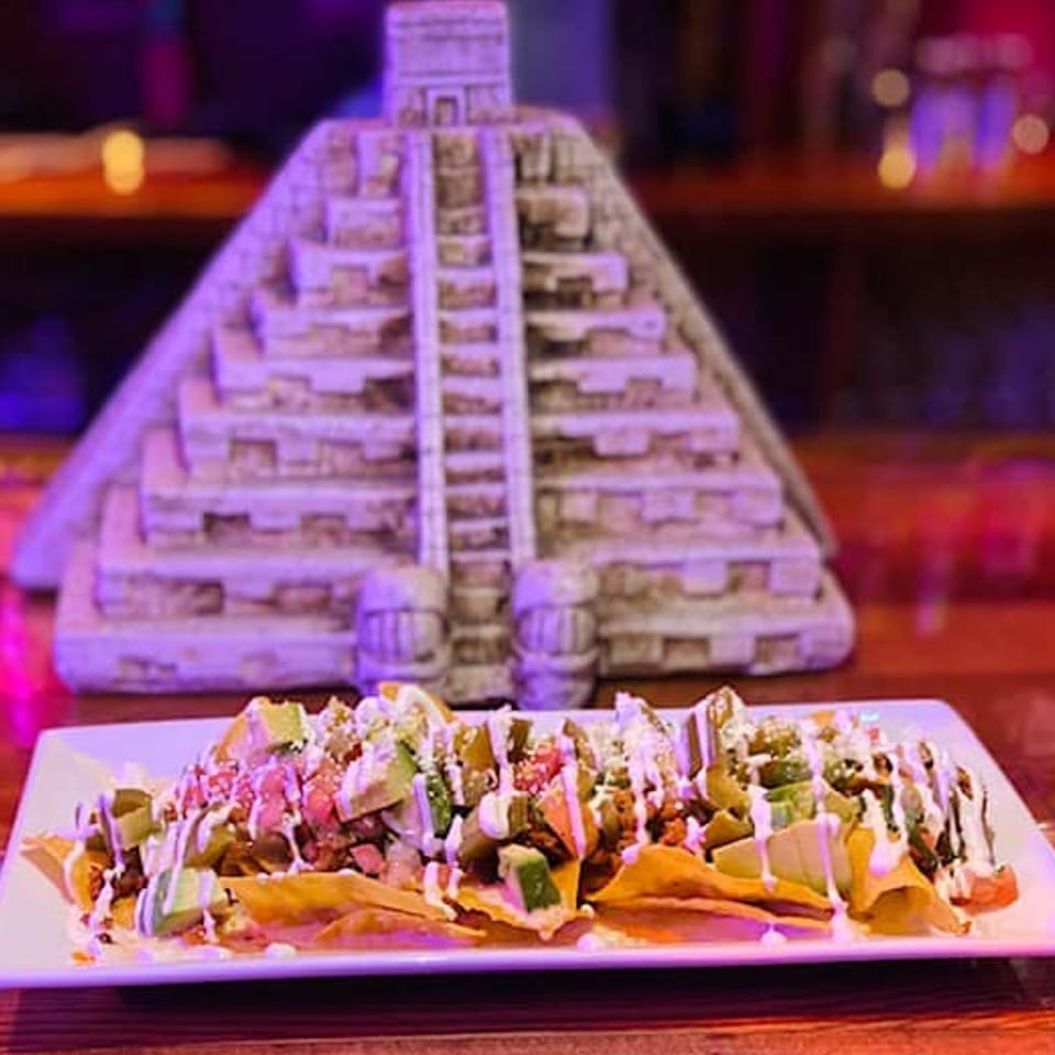 El Rey Azteca Mexican Restaurant's nachos with avocado, salsa, and sour cream, in front of a Mayan pyramid model.