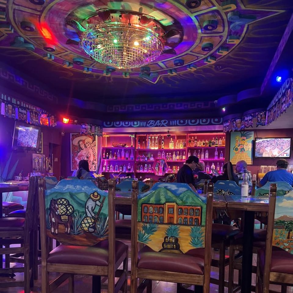 Vibrant Mexican restaurant interior with a disco ball, colorful lighting, and hand-painted chairs.